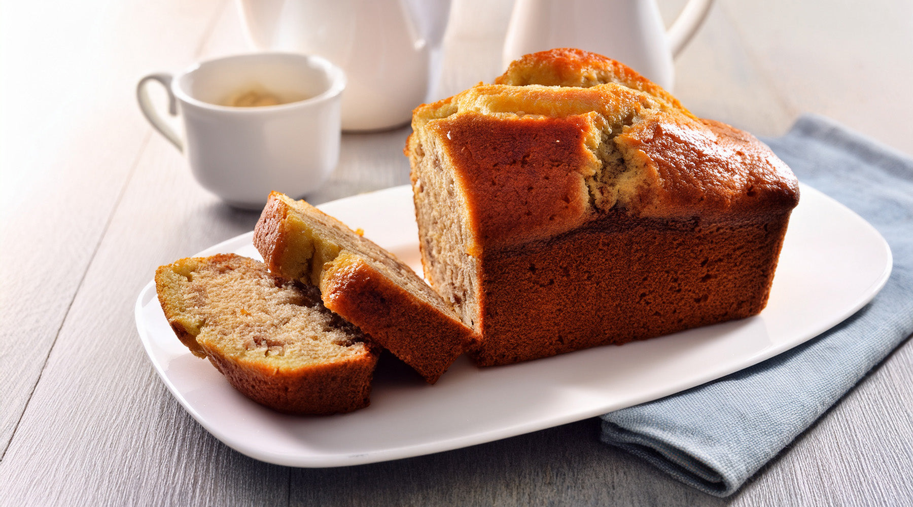 Sliced banana bread on a white plate with a coffee cup in the background