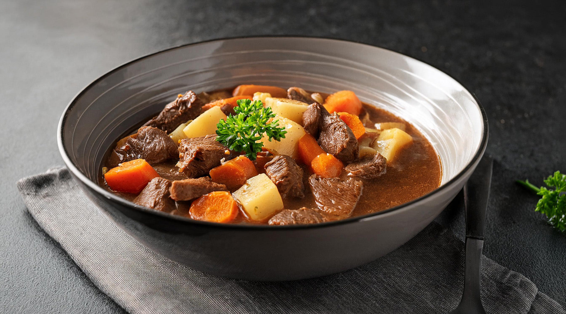 Beef stew in a white glass bowl on a black countertop