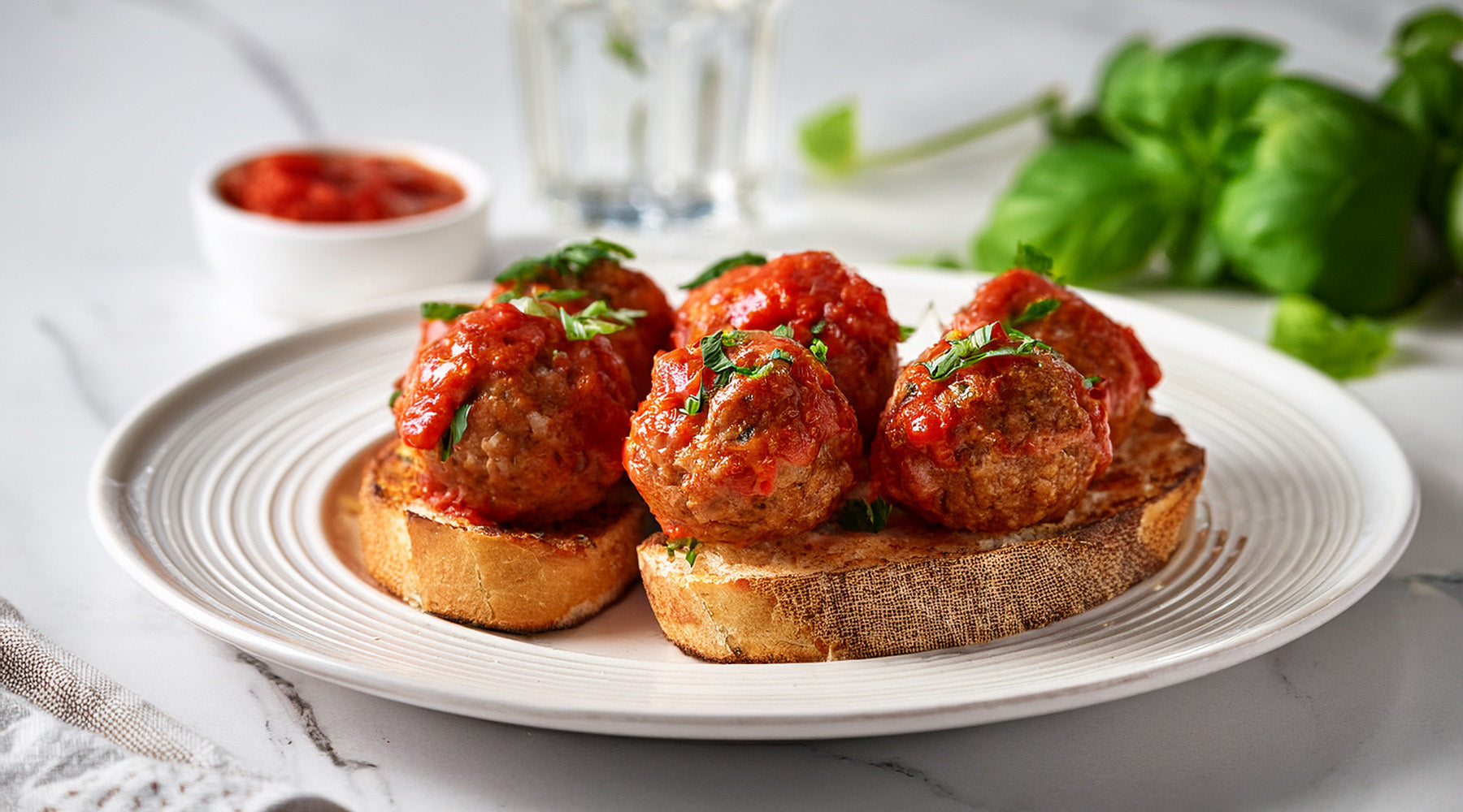Italian meatballs topped with tomato sauce on toasted bread on a white plate on a white marble countertop
