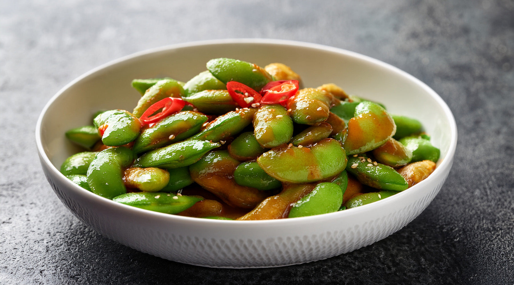 Edamame tossed in chili sauce in a white bowl