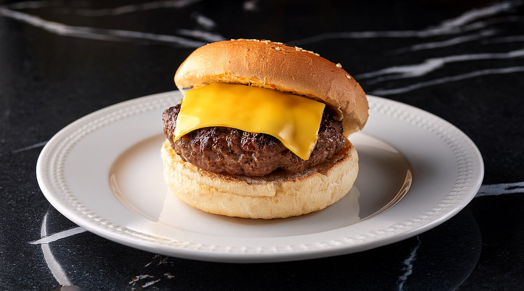 Steak burger with a slice of cheese on a white plate sitting on a black marble countertop