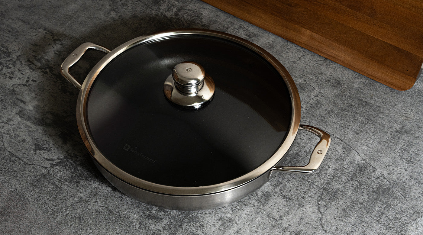 Nonstick Clad with tempered glass lid next to cutting board on top of a marble kitchen counter
