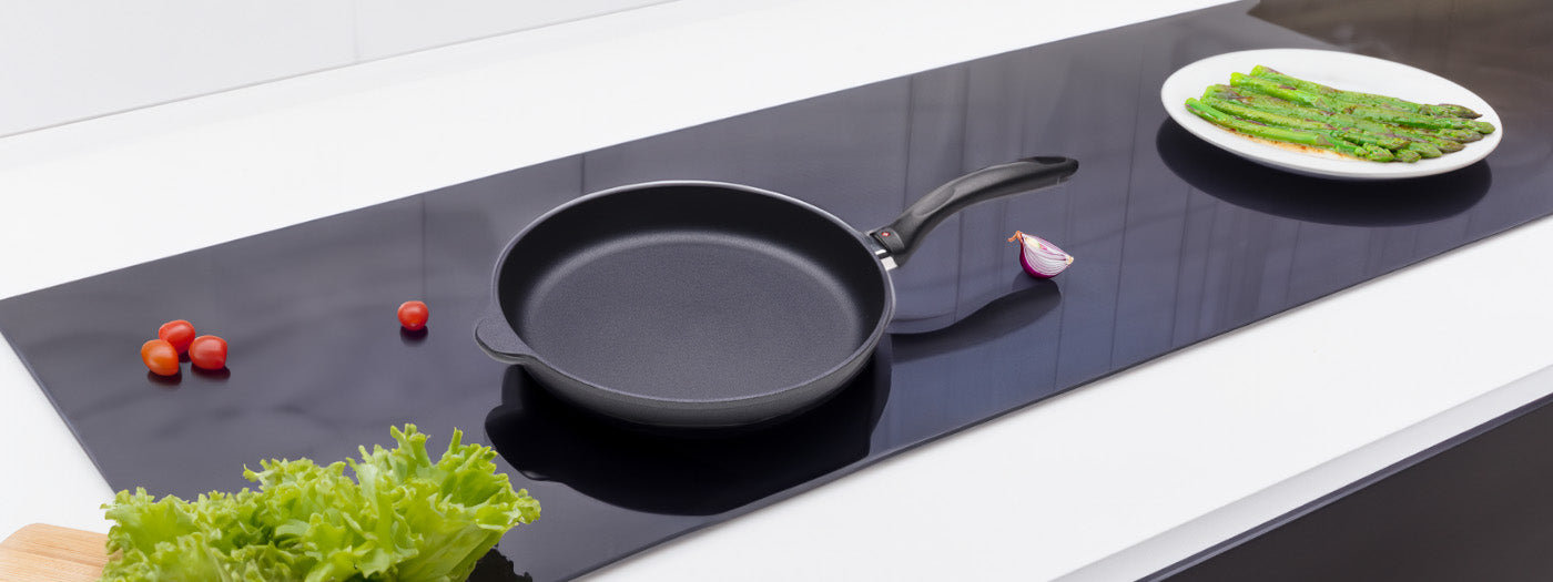 hd fry pan on flat glass stove top with a plate of veggies