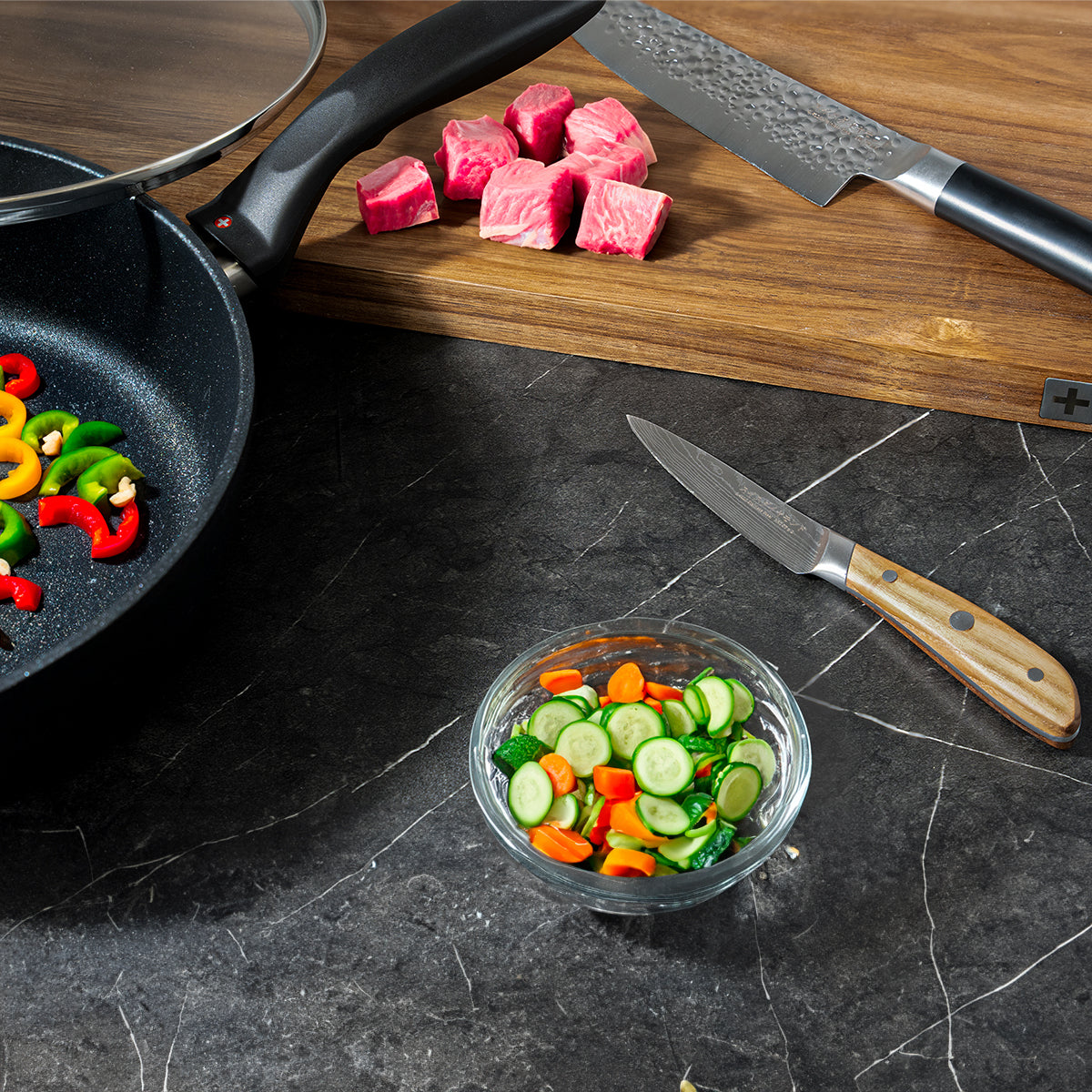 Knives on cutting board with chopped meat and fry pan with veggies in a bowl