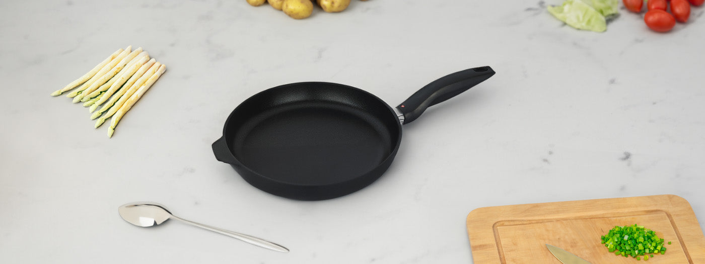 xd fry pan sitting on counter wit veggies and cutting board