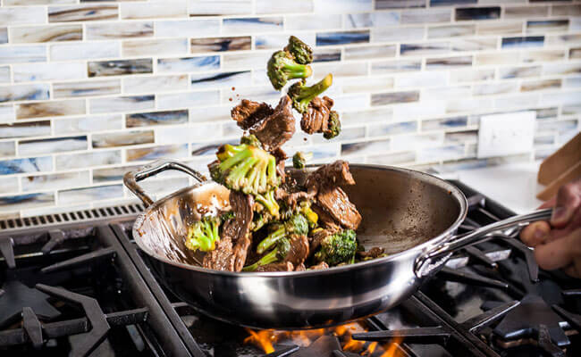 stainless steel fry pan over a gas stove with food being tossed inside