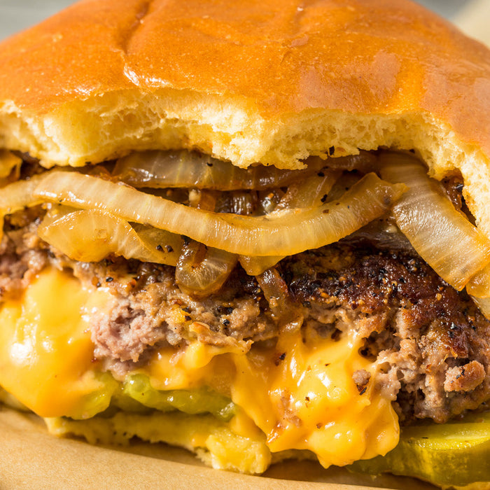 Burger with cheese in the middle, topped with onions and pickles