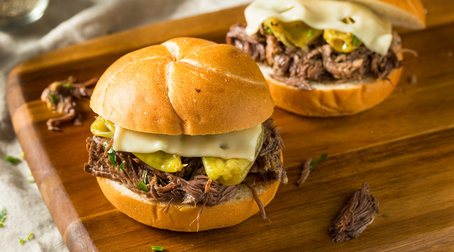 Shredded beef sandwiched in a kaiser roll topped with yellow pepperoncini peppers and cheese