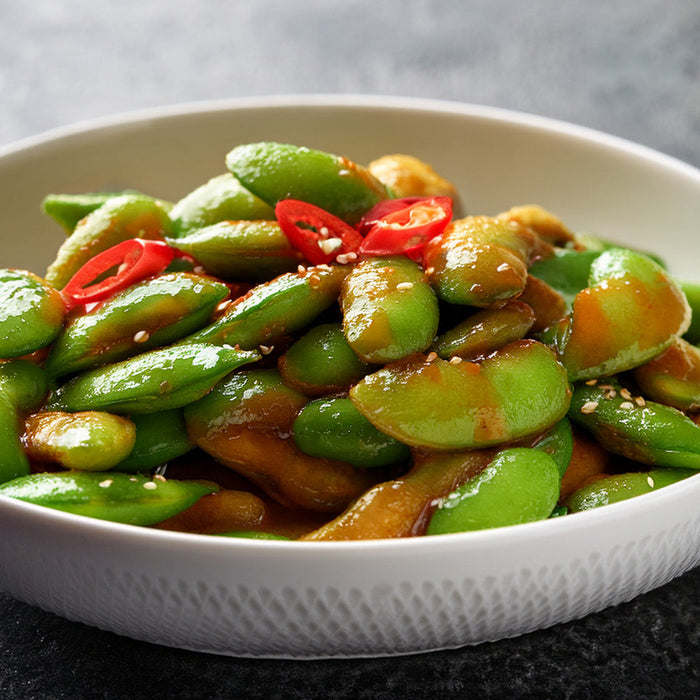 Edamame tossed in chili sauce in a white bowl