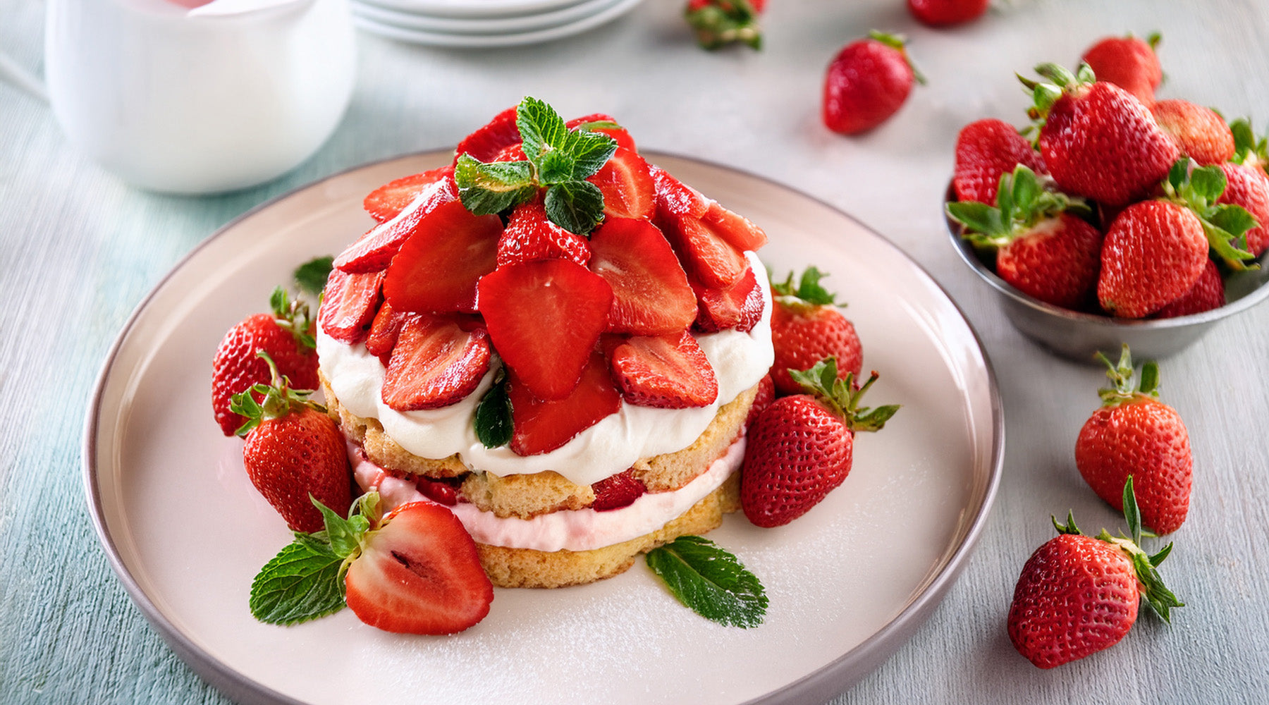 Strawberry shortcake on a white plate surrounded by fresh strawberries