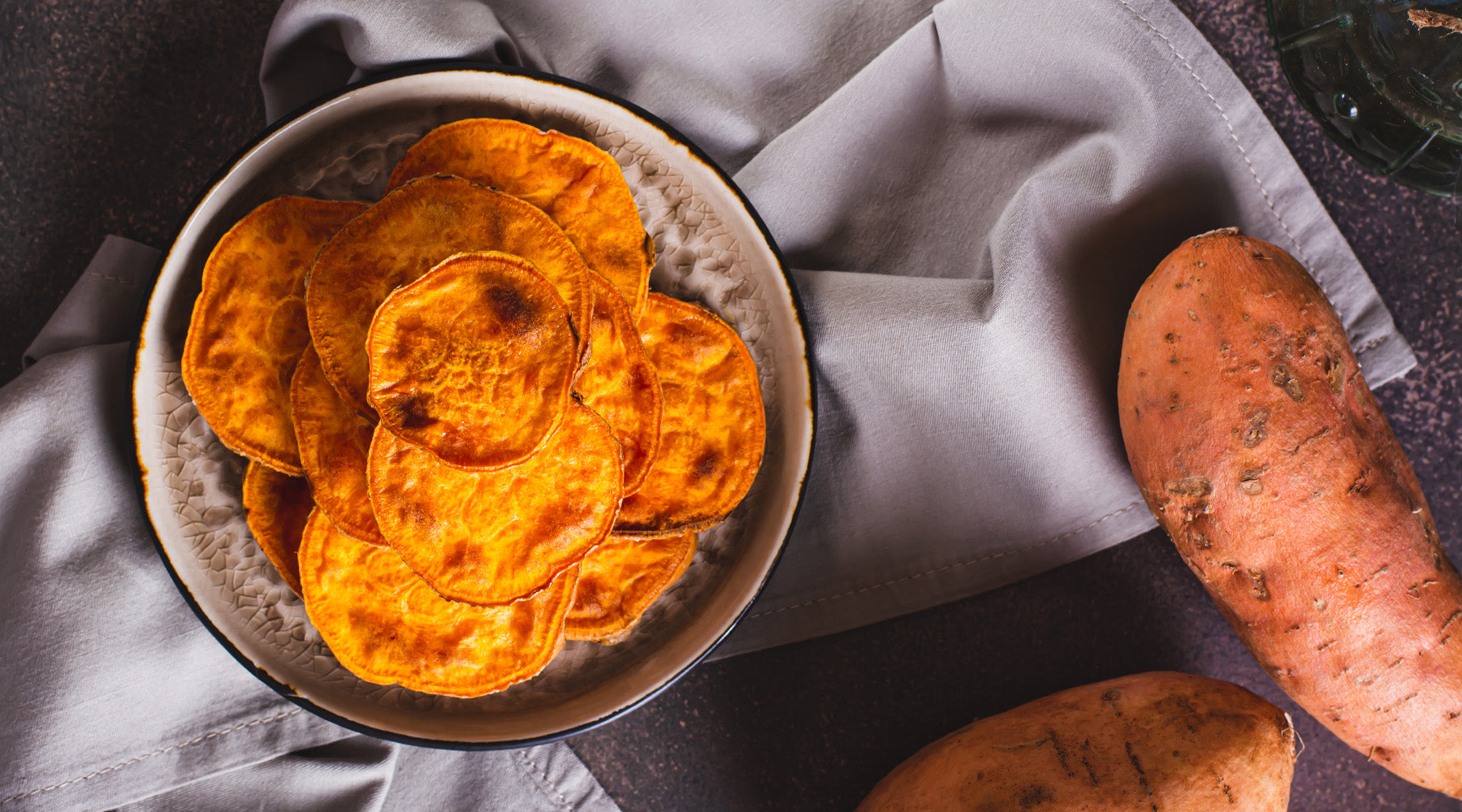 Sweet potato chips in a bowl on a counter top with whole sweet potatoes on the side