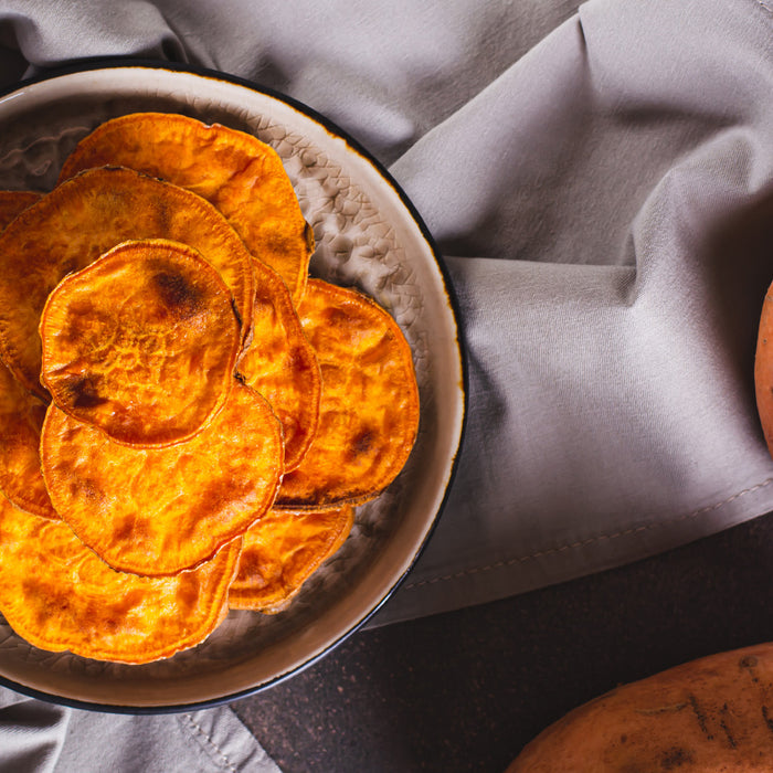 Sweet potato chips in a bowl on a counter top with whole sweet potatoes on the side
