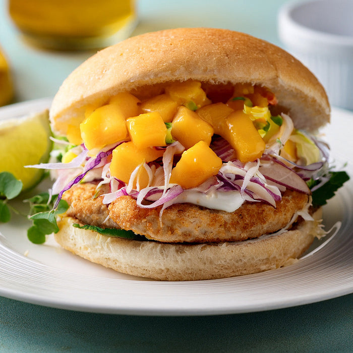 Turkey burger on a toasted bun topped with mango slaw on a white plate