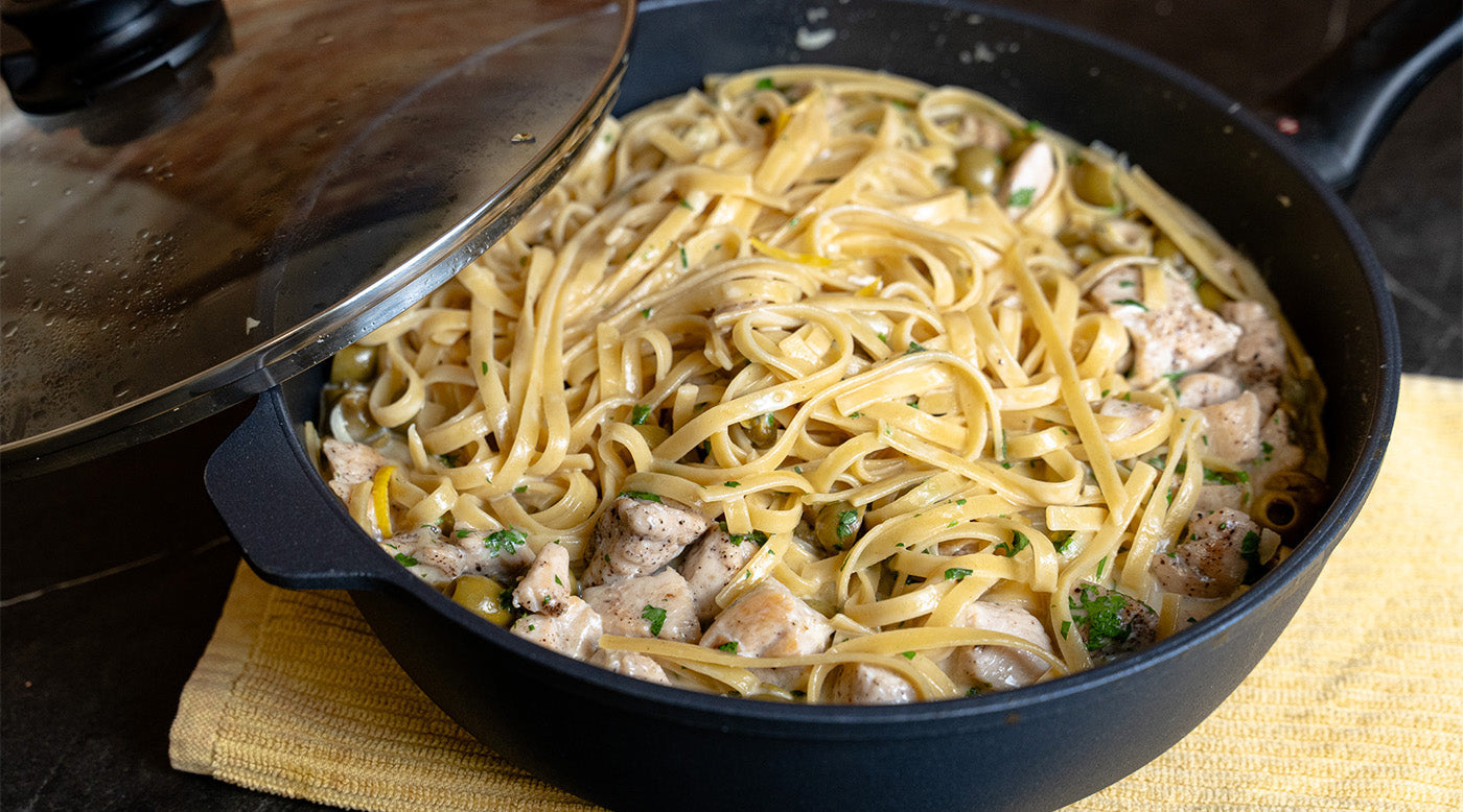 Nonstick sauté pan with glass lid and food inside on towel and kitchen counter