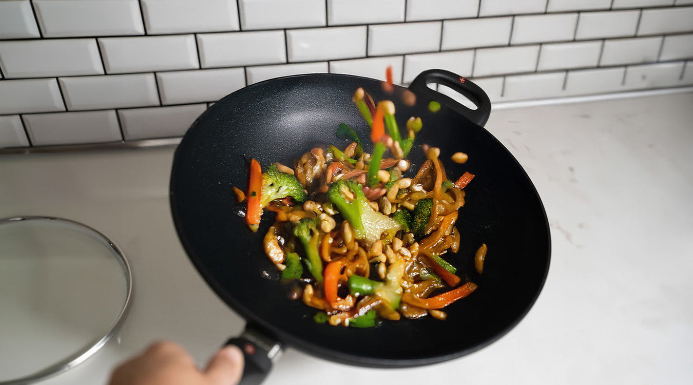 Woks & Stir Fry Pans with food inside and glass lid on top of white kitchen counter