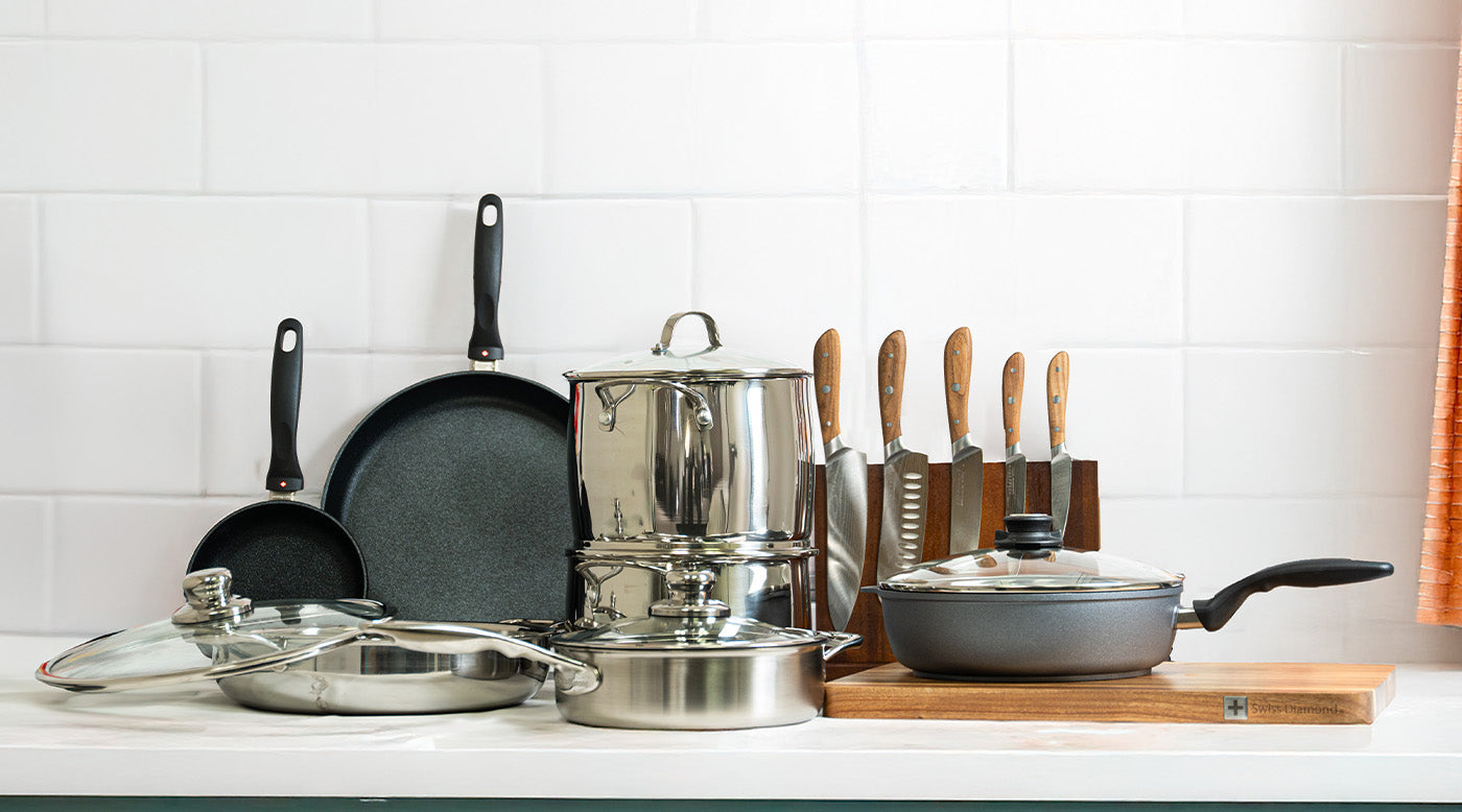 set of cookware including fry pans, saute pans, knives and dutch oven on white kitchen counter