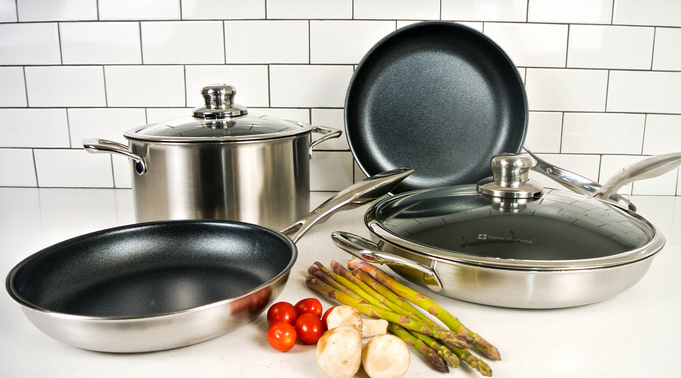 Stainless Steel Sets with food next to it and cookware including fry pan, dutch oven, and saute pan on white marble kitchen counter