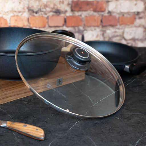 Tempered 12.5" Glass Lid tilted on side of pan on cutting board and kitchen counter top