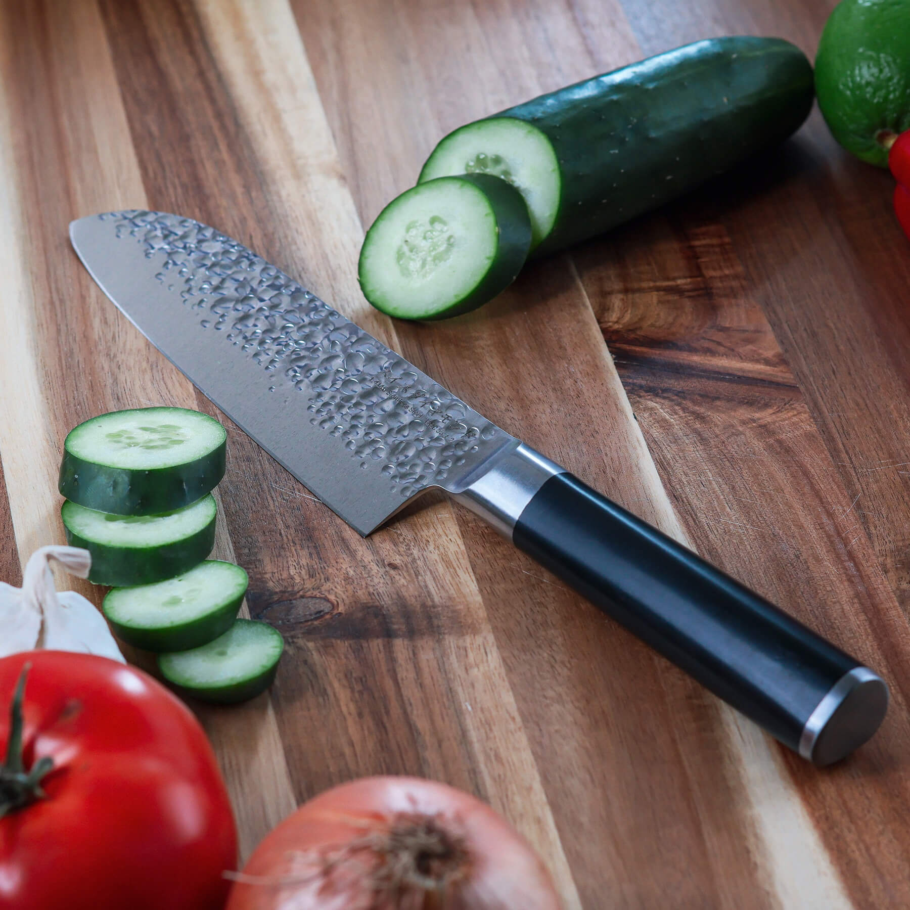7" Hammered Santoku Knife on cutting board with sliced cucumbers