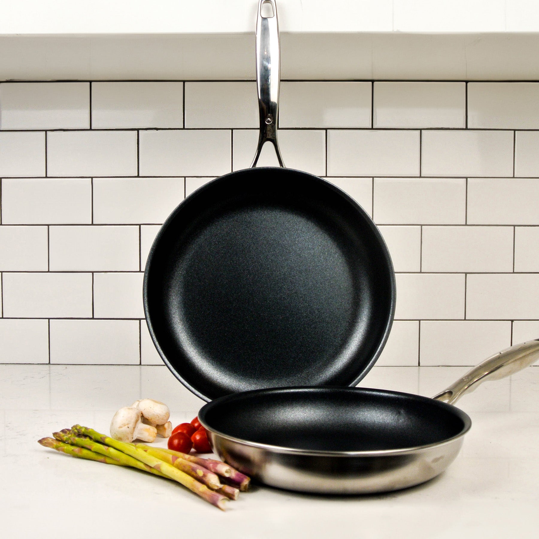 Nonstick Clad Fry Pan 2-Piece Set - Induction in use on a kitchen counter one pan is vertical and other is lying flat