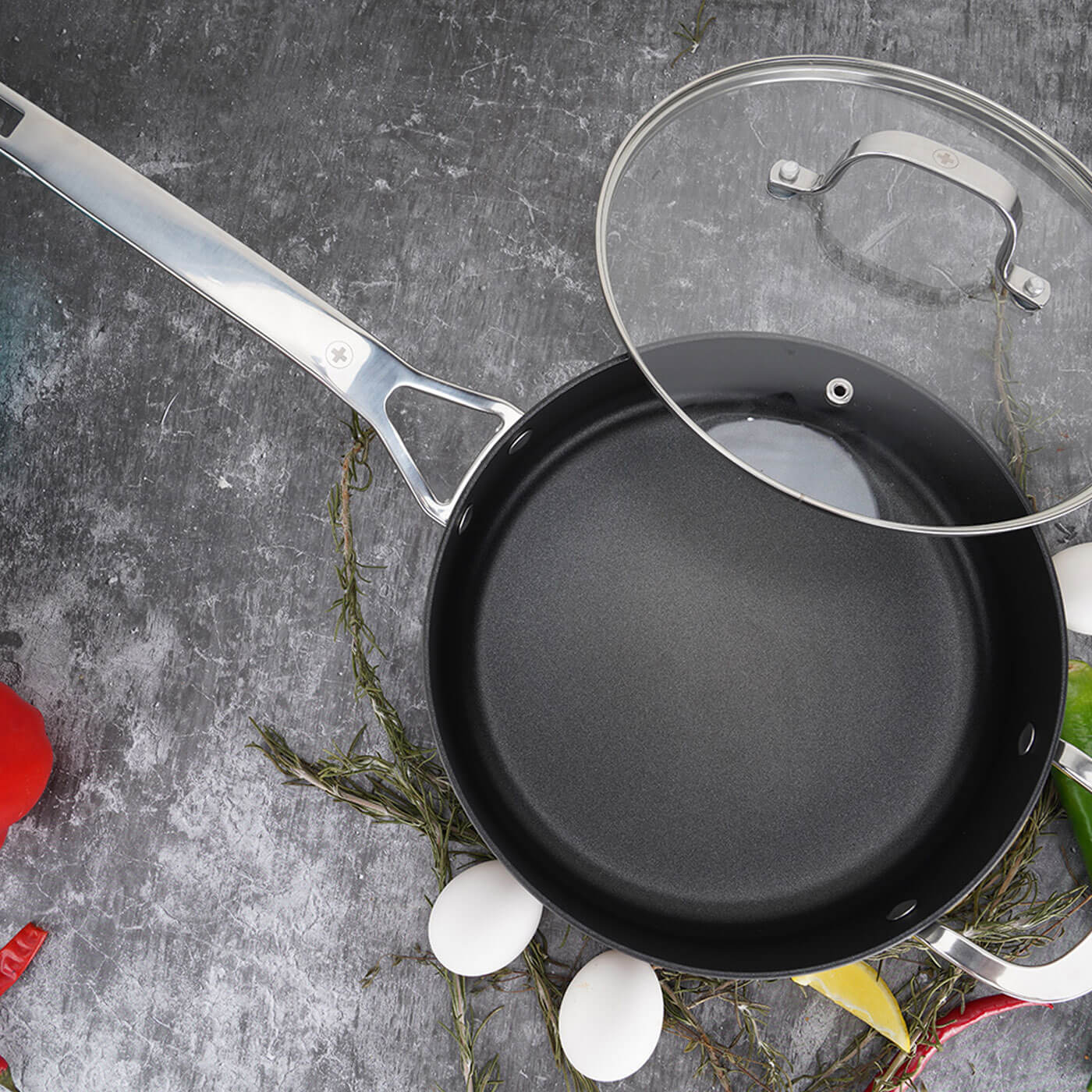 top view of hard anodized fry pan with glass lid and eggs next to it on marble counter