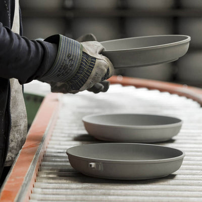 factory worker handling unfinished fry pans on a conveyer belt