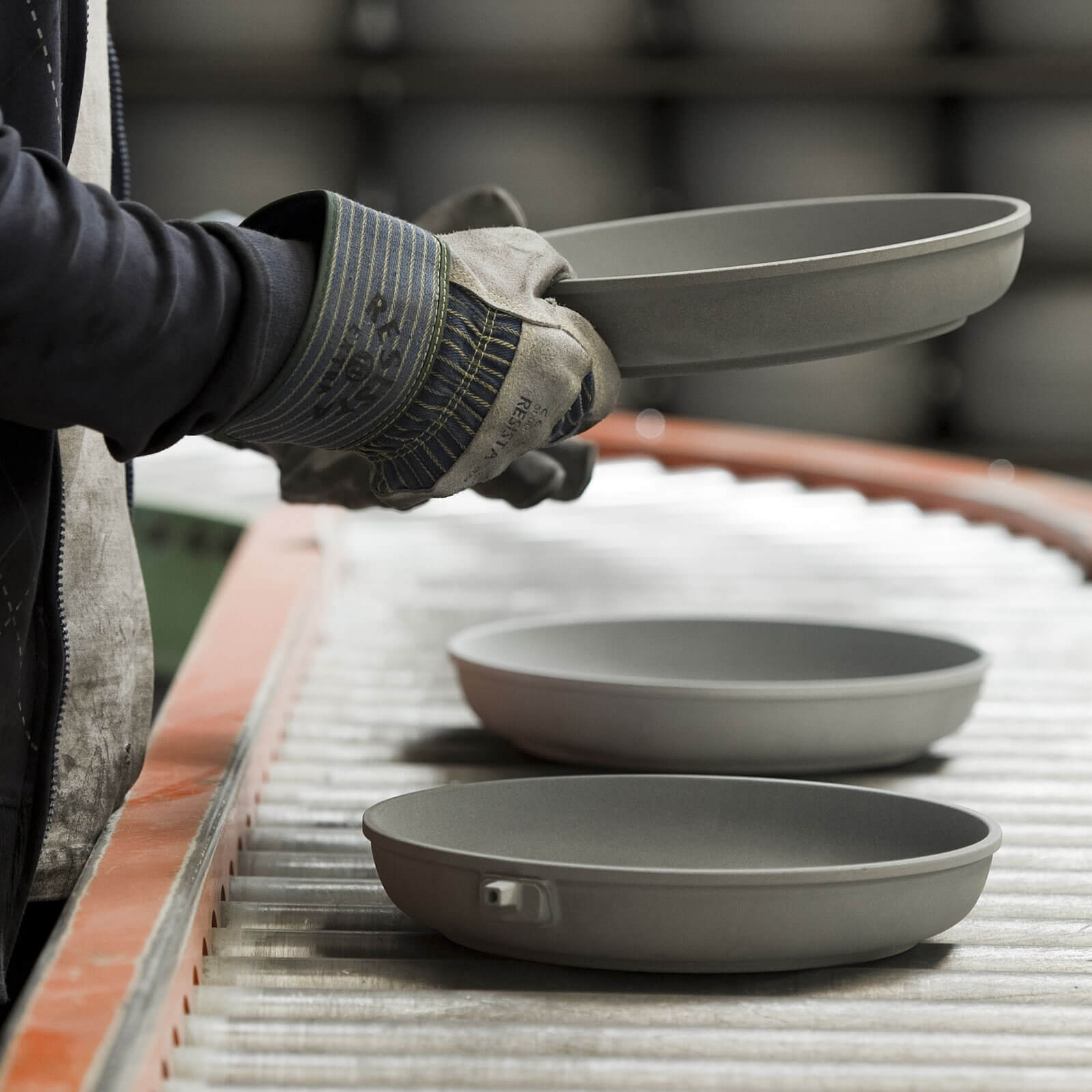 a factory worker handling a mold of an unfinished fry pan on conveyer belt